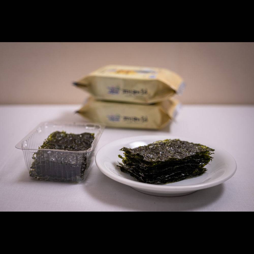 a white plate topped with seaweed next to a container of seaweed